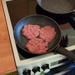 Na patelni smażą się trzy kotlety z mięsa mielonego na kuchence.