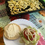 Na talerzu jest składany burger, a w tle blacha z frytkami.