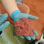 Na zdjęciu widać uformowany kotlet z mięsa mielonego trzymany w rękawiczkach nad stołem.