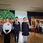 Uczniowie recytują wiersze. W tle na ekranie projekcyjnym powiewa flaga biało-czerwona..jp.jpg