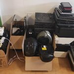 Na zdjęciu znajdują się poukładane przy ścianie kartony i stosy używanego sprzętu AGD i elektronicznego. Widać  m.in małe urządzenia kuchenne, odtwarzacze, głośniki, drukarki, tablety i laptopy. 