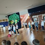 Uczniowie klasy 1D podczas występu z okazji Święta Szkoły w Szkole Podstawowej nr 12 im. Zygmunta Glogera w Białymstoku. Dzieci stoją na szkolnej scenie z przygotowanymi dekoracjami.