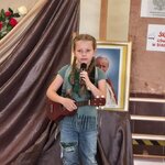 Dziecko stoi na scenie_ trzyma  ukulele i śpiewa do mikrofonu w tle portret Jana Pawła II_.jpg