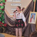 Dziewczynka w ludowej bluzce i spódnicy w róże śpiewa do mikrofonu na scenie z napisem „Re.jpg