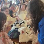 Kobieta w niebieskiej marynarce i dzieci stoją wokół stołu z pluszowymi owieczkami. W tle .jpg