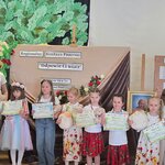 Grupa dzieci z dyplomami i maskotkami oraz trzy dorosłe kobiety pozują do zdjęcia na tle d.jpg
