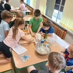 Dzieci pracują przy stoliku_ ugniatają i wałkują ciasto na blacie miska_ mąka_ butelka oli.jpg