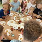 Grupa dzieci otacza stół z talerzami pełnymi ciasteczek dzieci wybierają i jedzą wypieki w.jpg