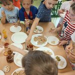 Dzieci stoją przy stole w klasie_ sięgają po krakersy z talerzy i nakładają dodatki z mały.jpg