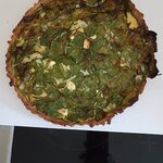 Okrągła wytrawna tarta ze szpinakiem i kawałkami sera leży na białej desce na płycie grzew.jpg