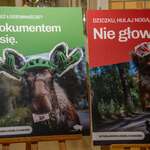 Dwa plakaty ustawione na sztalugach w holu szkoły przedstawiają dzikie zwierzęta w kaskach ochronnych, a nad nimi widoczne są hasła: „Z dokumentem da się” oraz „Nie głowa”. W dolnej części plakatów znajduje się napis „W Podlaskiem jeżdżę z kaskiem”.