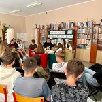 widok na regały z książkami_ zgromadzone osoby słuchają czytanego tekstu.jpeg