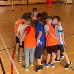 Grupa dzieci stoi w kręgu na sali gimnastycznej podczas zajęć sportowych.