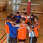  Dzieci stoją w kręgu na sali gimnastycznej, przygotowując się do wspólnej aktywności sportowej.