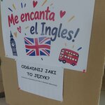 Plakat promujący język angielski z napisem „Me encanta el Ingles!” oraz grafikami przedstawiającymi brytyjską flagę, Big Bena i czerwony autobus. Poniżej informacja o zabawie „Odgadnij jaki to język?”.