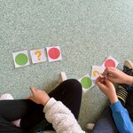 Dwoje dzieci siedzi na podłodze i układa karty z kolorowymi kołami, uzupełniając sekwencję według wzoru.