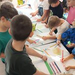 Grupa dzieci przy wspólnych stołach rysuje kredkami i ołówkami. Na blatach kartki_ kleje i.jpg