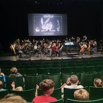 Orkiestra na scenie przed koncertem_ na duzym ekranie nad muzykami wyświetlony tytuł nieme.jpg