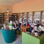 Uczniowie zanurzeni w lekturze podczas wizyty w bibliotece szkolnej. W tle widoczne są regały z książkami dla dzieci i młodzieży.