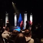 widzowie siedzą na krzesłach w oddali oświetlona scena