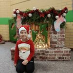 Chłopiec ubrany w świąteczny sweter oraz czapkę mikołaja siedzi na dywanie i pozuje do zdj.jpg