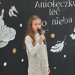 Dziewczynka trzyma mikrofon na tle napisu Aniołeczku leć do nieba.jpg