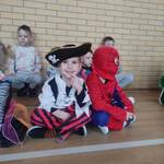 Dwóch chłopców przebranych za pirata i Spidermana siedzą w siadzie skrzyżnym podczas zabawy choinkowej...jpg