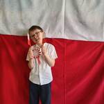 Chłopiec z grupy Żabki trzyma w rękach dwie Flagi Polski pozując na tle ścianki patriotycznej..jpg