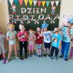 Grupka dzieci z grupy Misie z rekwizytami na tle dekoracji z okazji Dnia Przedszkolaka.jpg