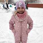 Dziewczynka z grupy Biedronki w różowym kombinezonie w gwiazdki pozuje do zdjęcia na tle zimowego krajobrazu szkolnego..jpg