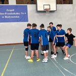 Grupa chłopców w niebieskich strojach meczowych na sali gimnastycznej stojąca w kole przed początkiem meczu.